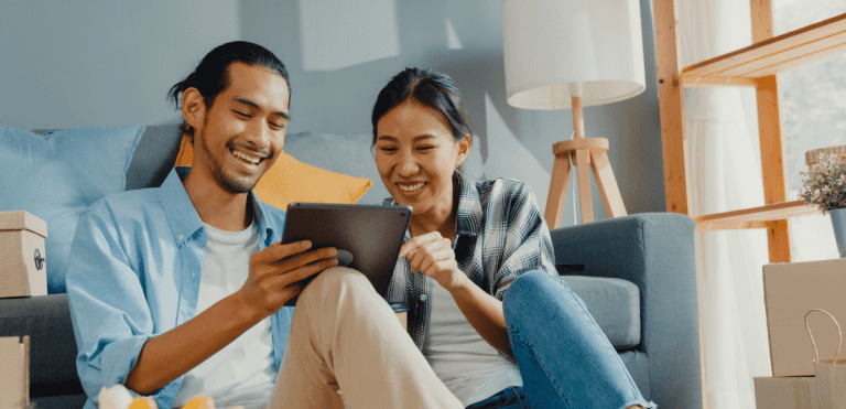 Two people sitting together on a sofa and looking at a tablet.