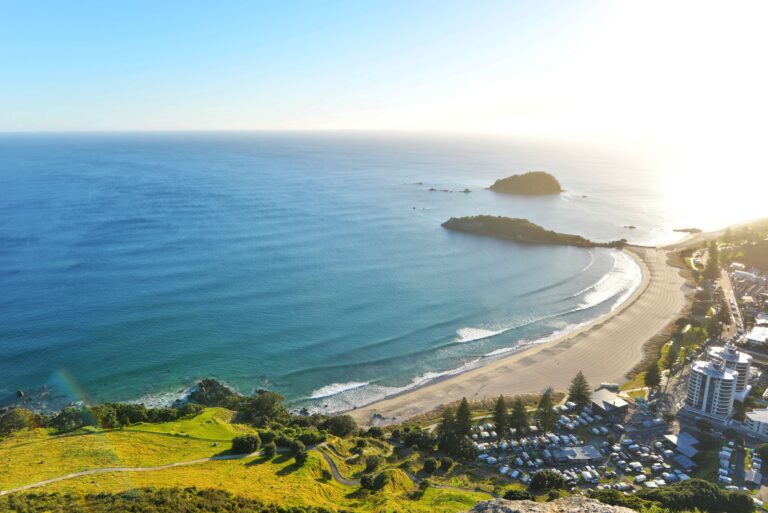 Coastal view over a curved sandy beach, ocean, small islands and waterfront buildings.