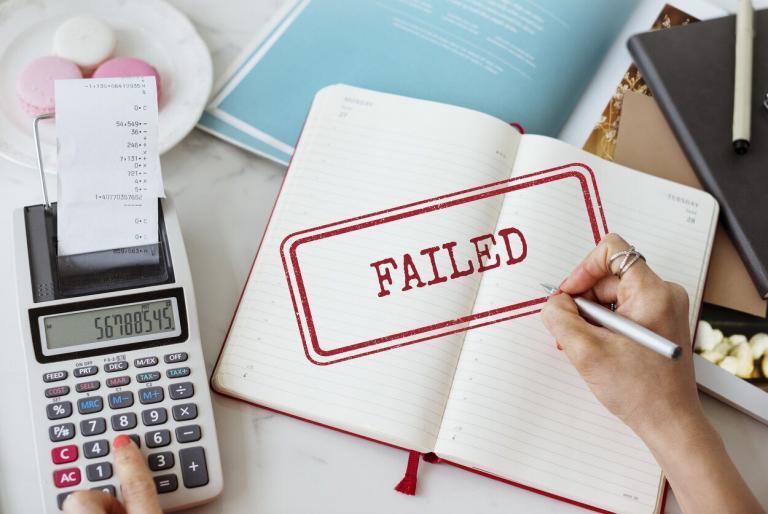 Hands using a calculator and holding a pen over a notebook marked FAILED.