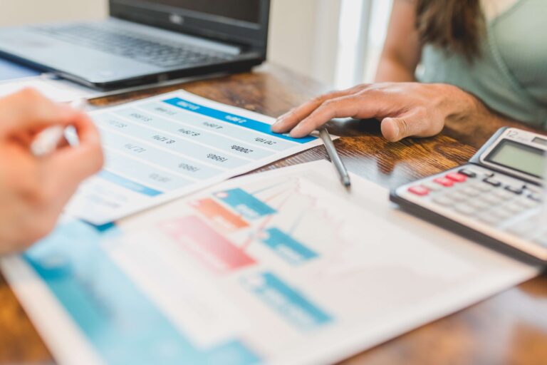 Two people reviewing printed figures and charts beside a laptop and calculator.